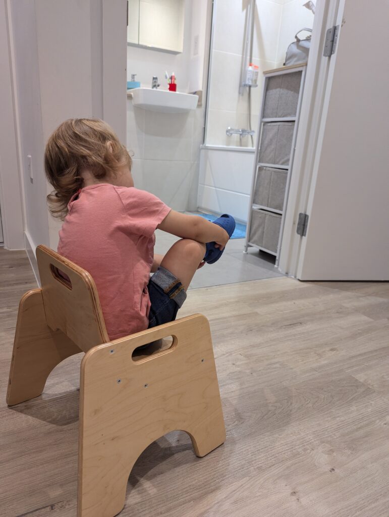 Zara mette le scarpe da sola seduta su una piccola sedia. Imparare a vestirsi da soli è una tappa importante dello sviluppo dei bambini