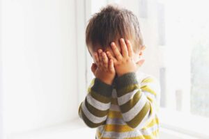 bambino timido si copre il viso con le mani