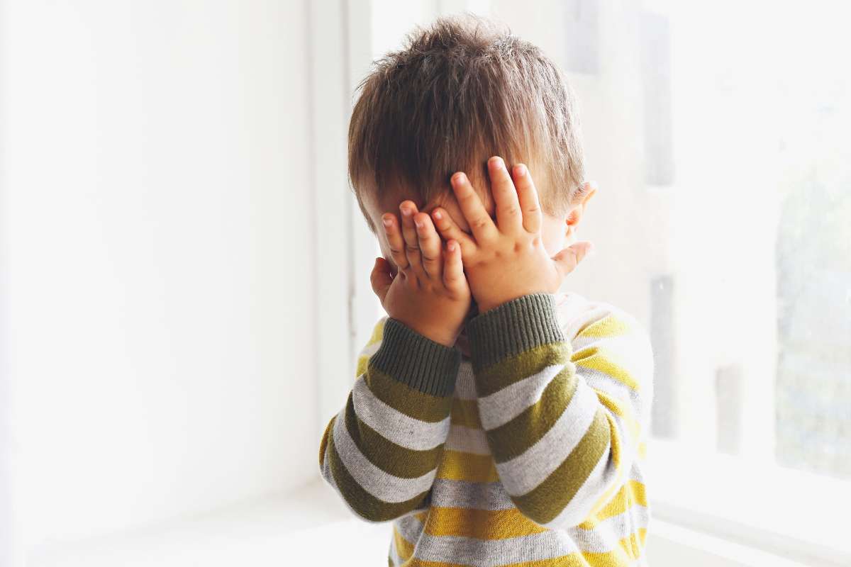 bambino timido si copre il viso con le mani