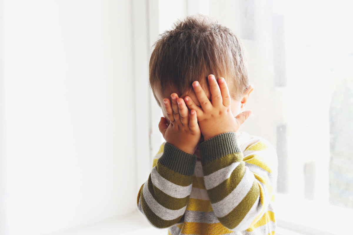 bambino timido si copre il viso con le mani
