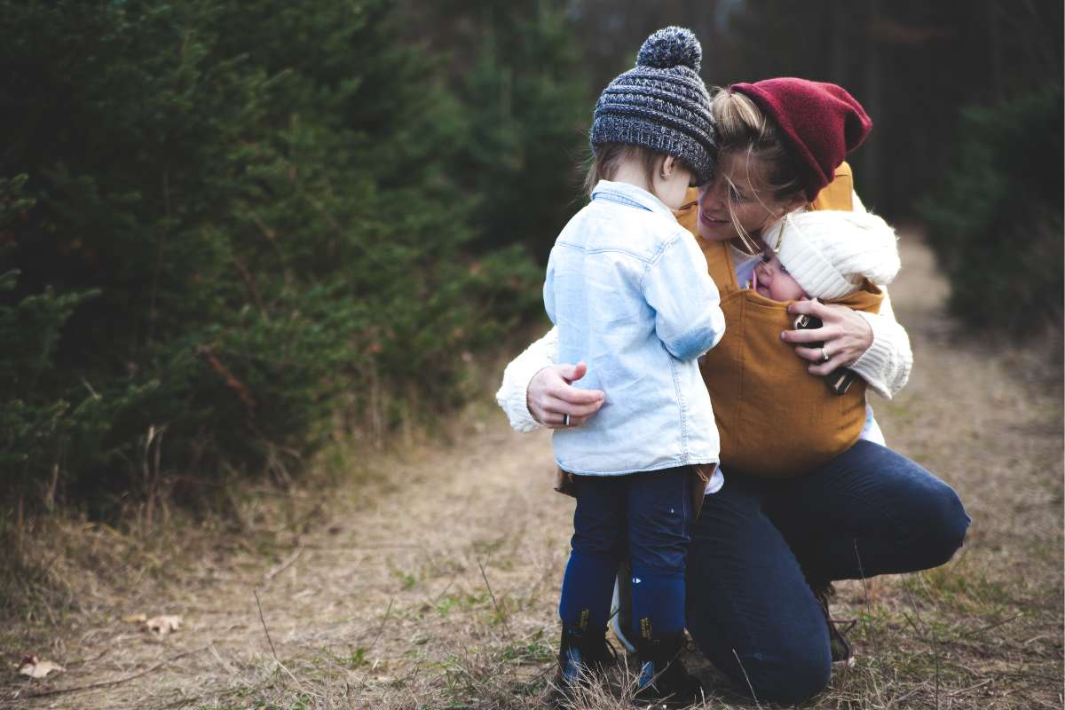 Mamma con due bambini di età diverse abbraccia entrambi