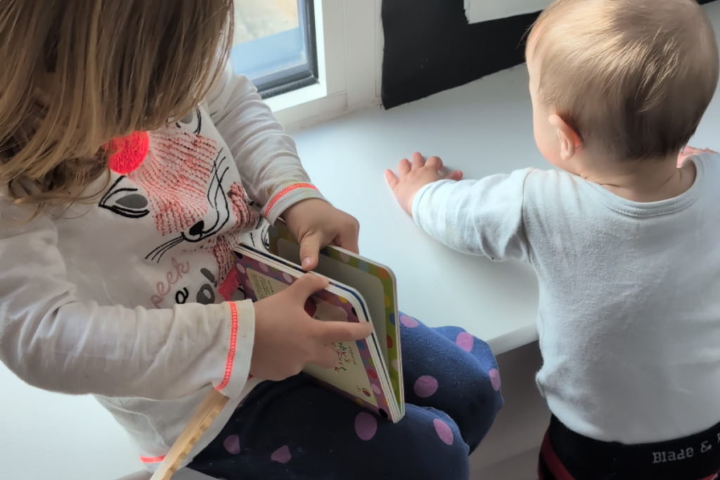 Bambina d i3 anni legge un libro con il fratellino piccolo