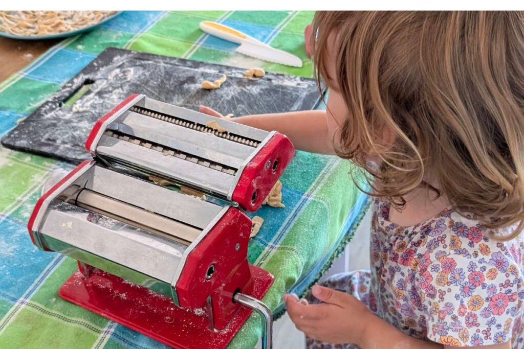 bambina che aiuta a fare la pasta fatta in casa con un impastatrice manuale